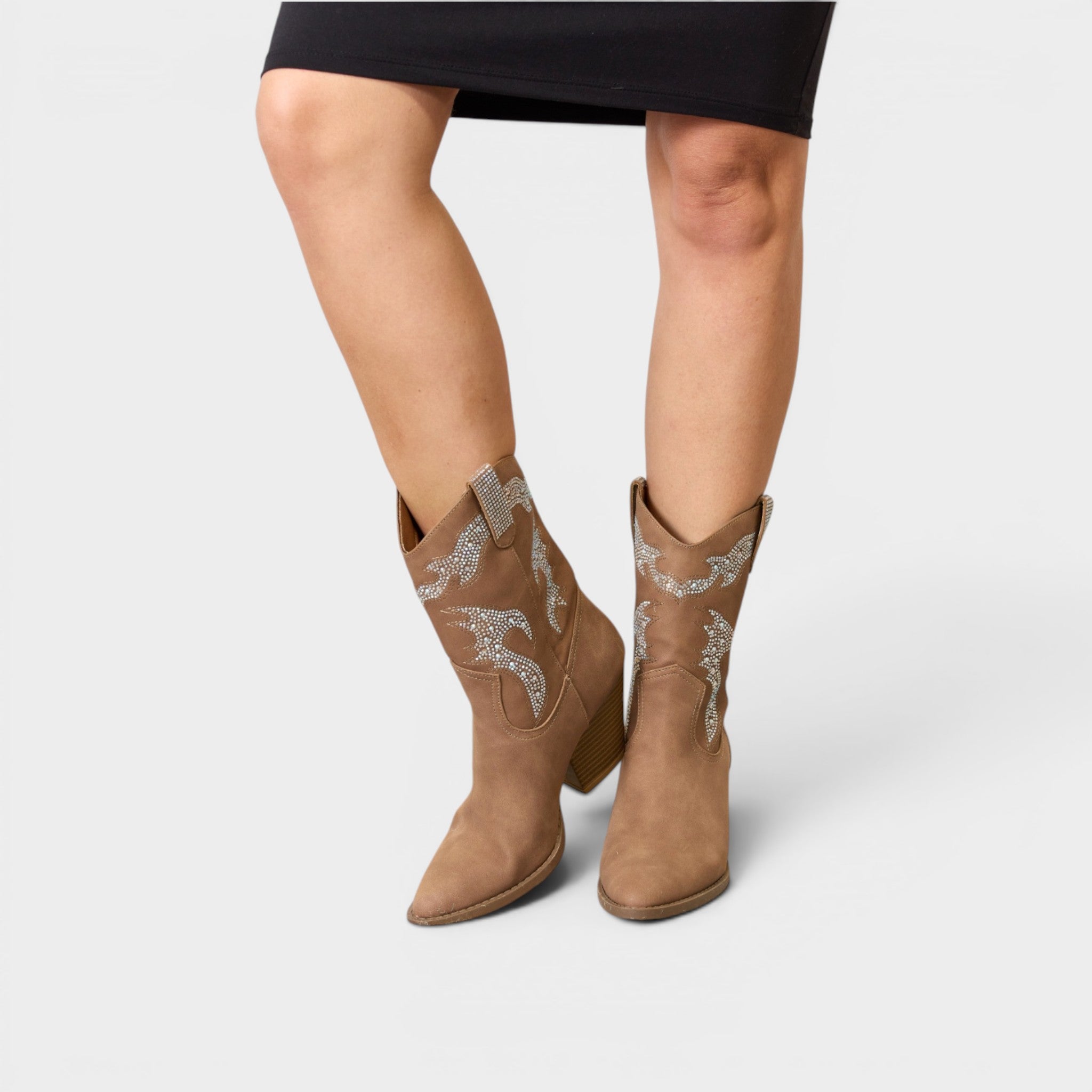 Brown cowboy boots with decorative patterns worn by a person on a white background