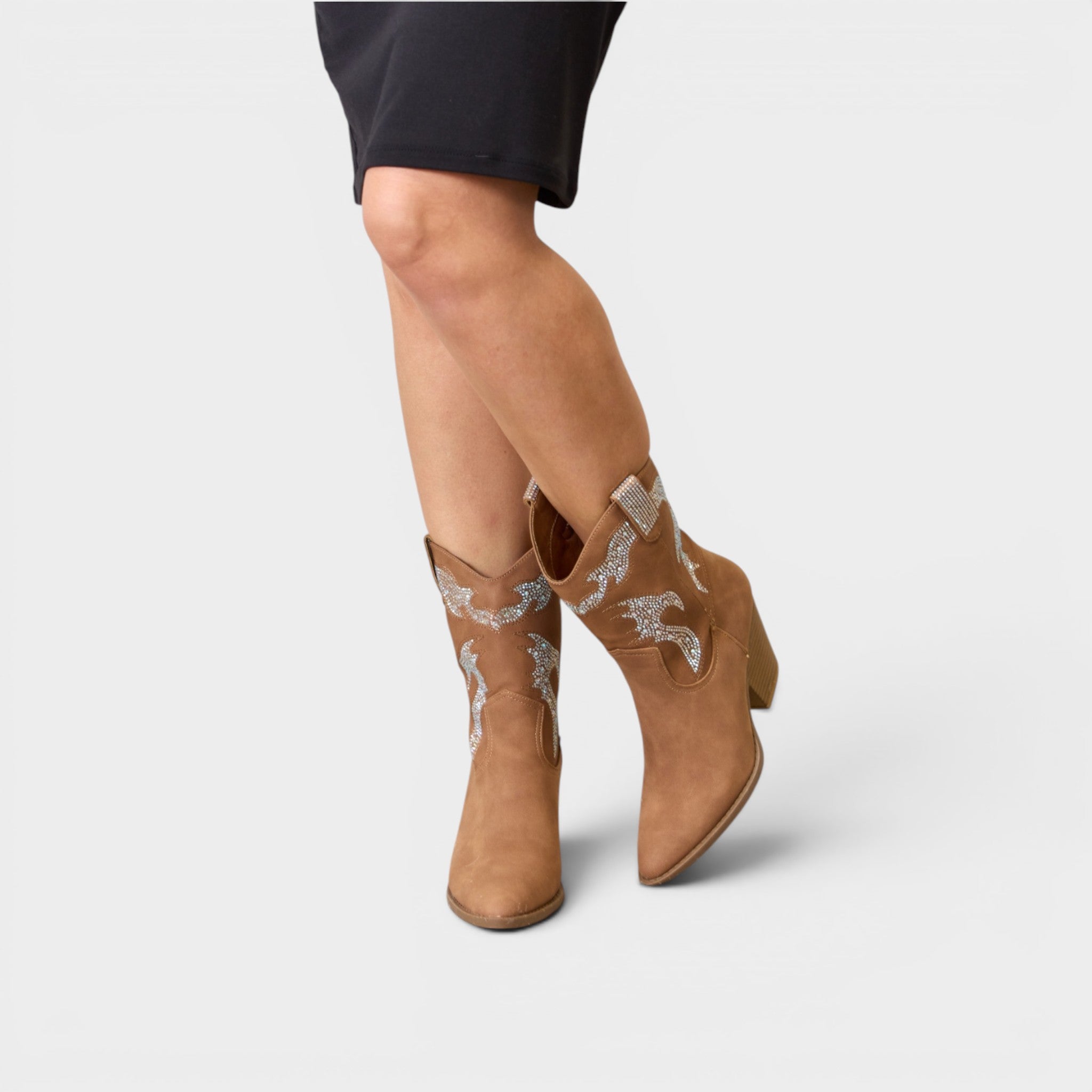 Tan cowboy boots with decorative patterns worn by a person on a light gray background