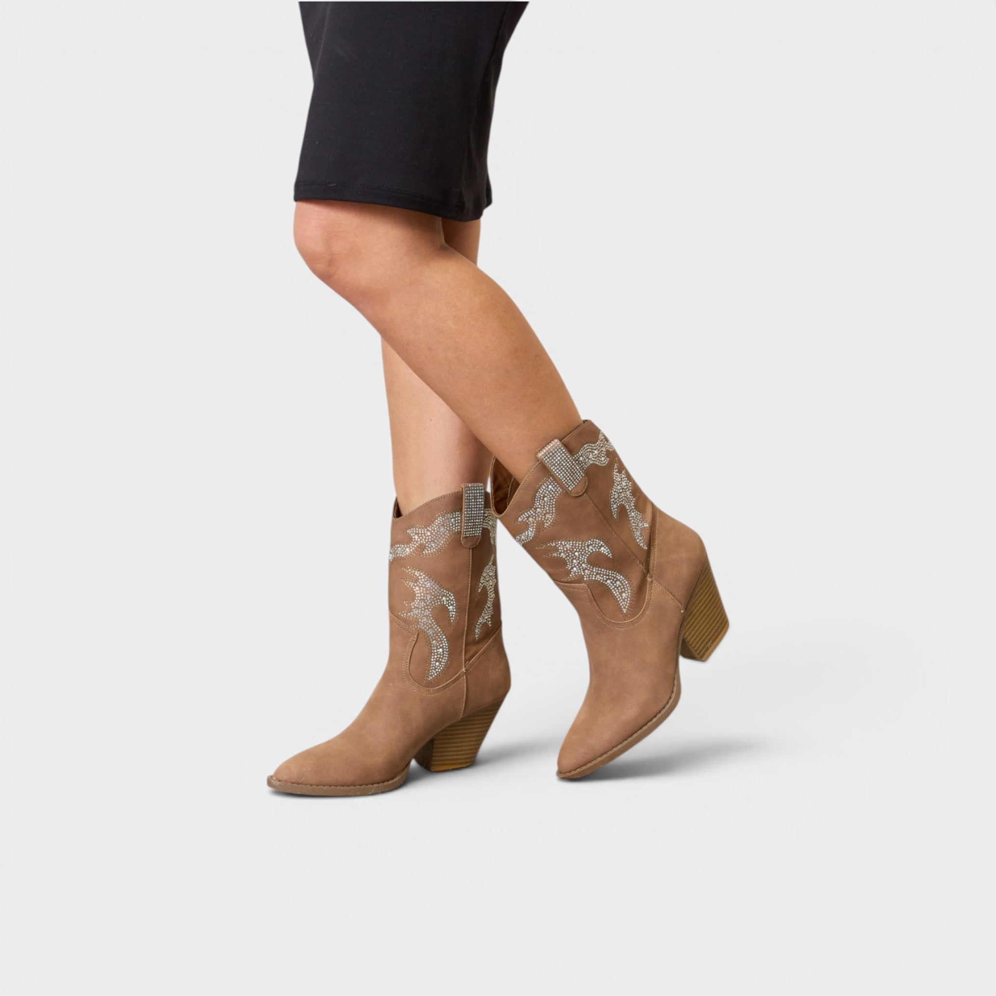 Tan ankle boots with decorative elements worn by a person on a light gray background