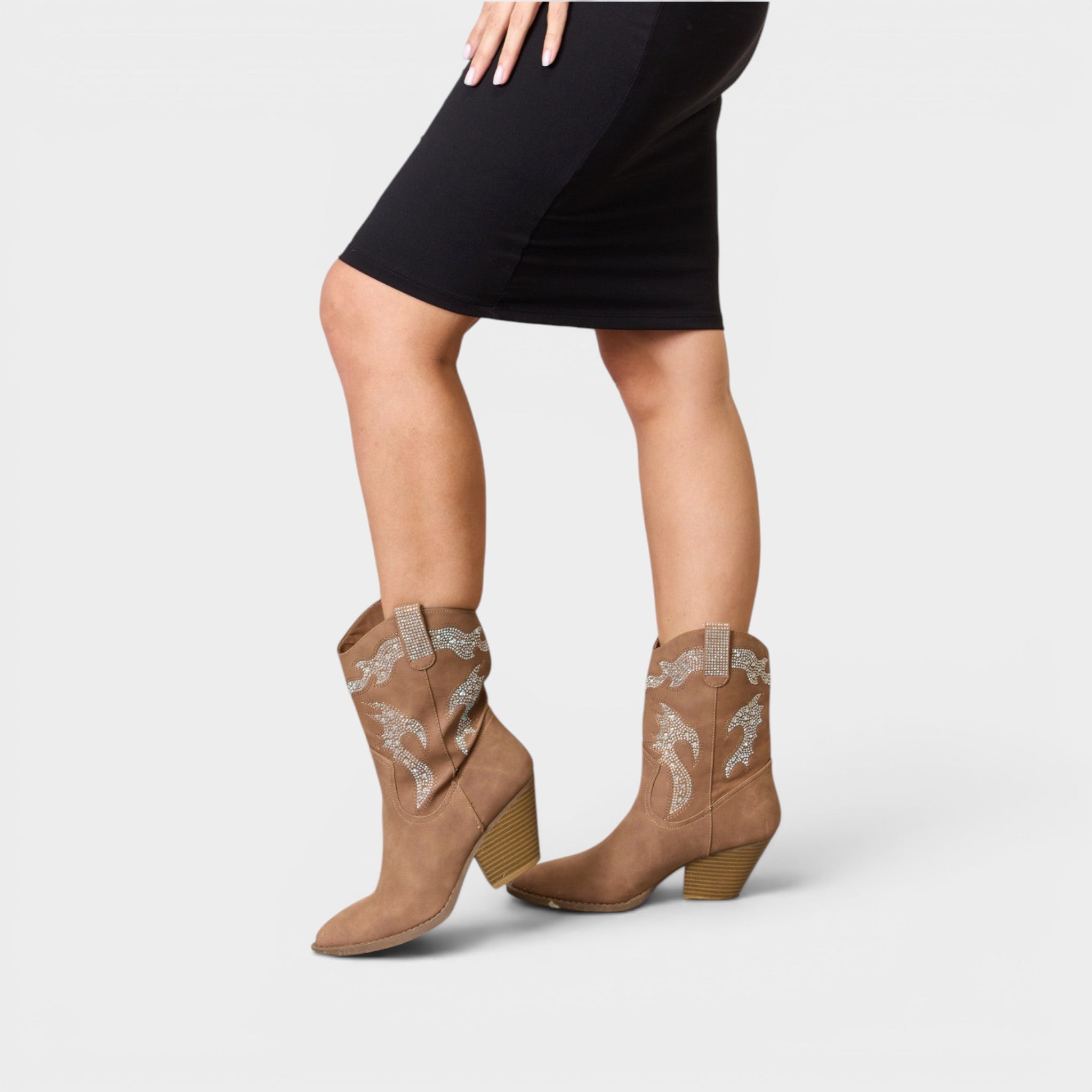 Tan cowboy boots with lace details worn by a person in a black dress on a light gray background