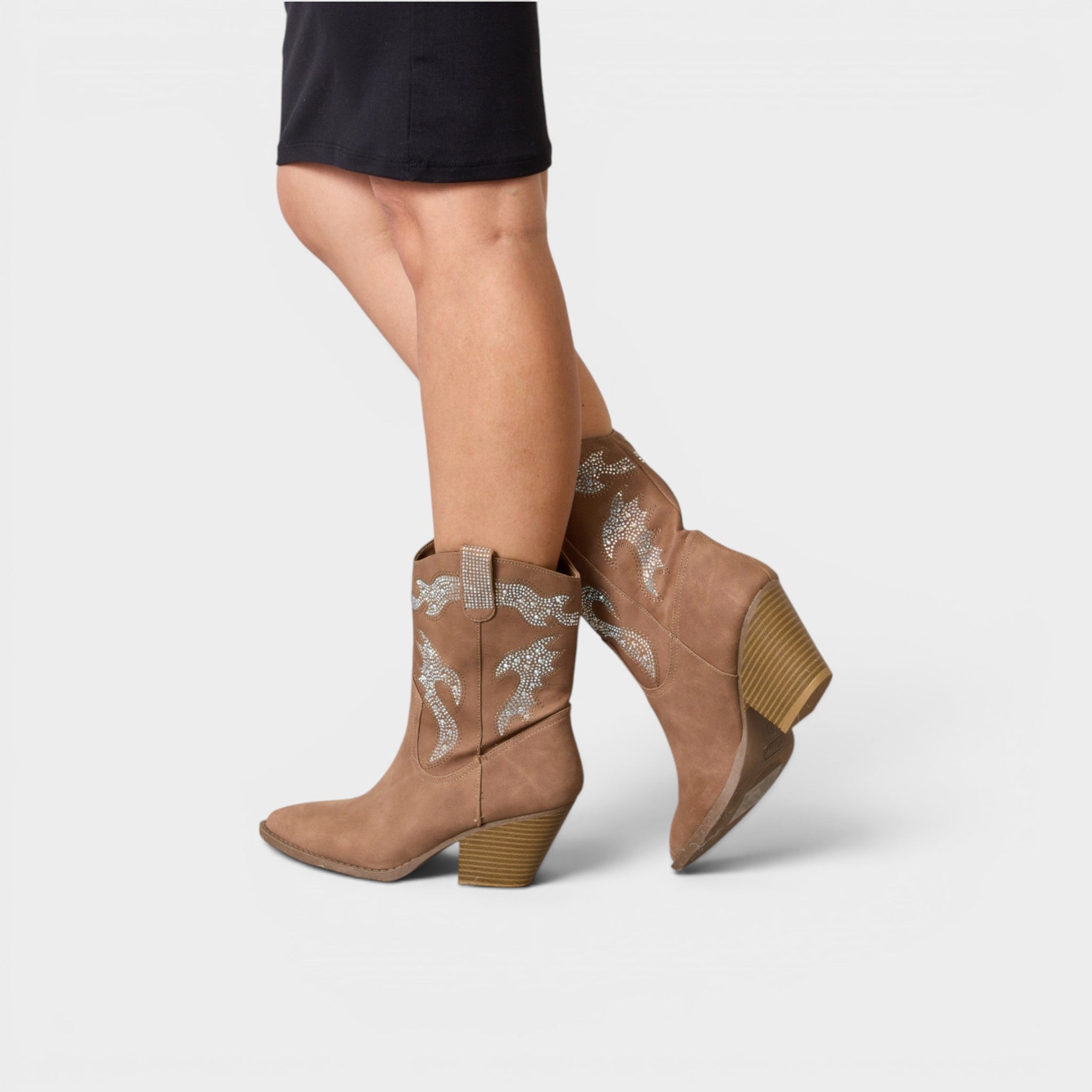 Tan ankle boots with decorative elements worn by a person on a white background