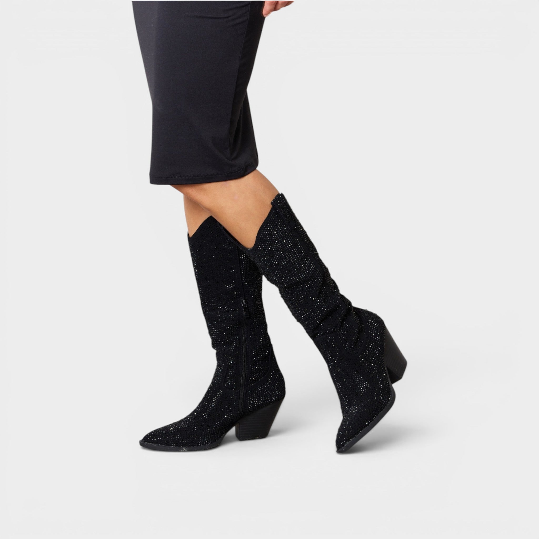 Black glittery knee-high boots worn with a black dress on a light gray background