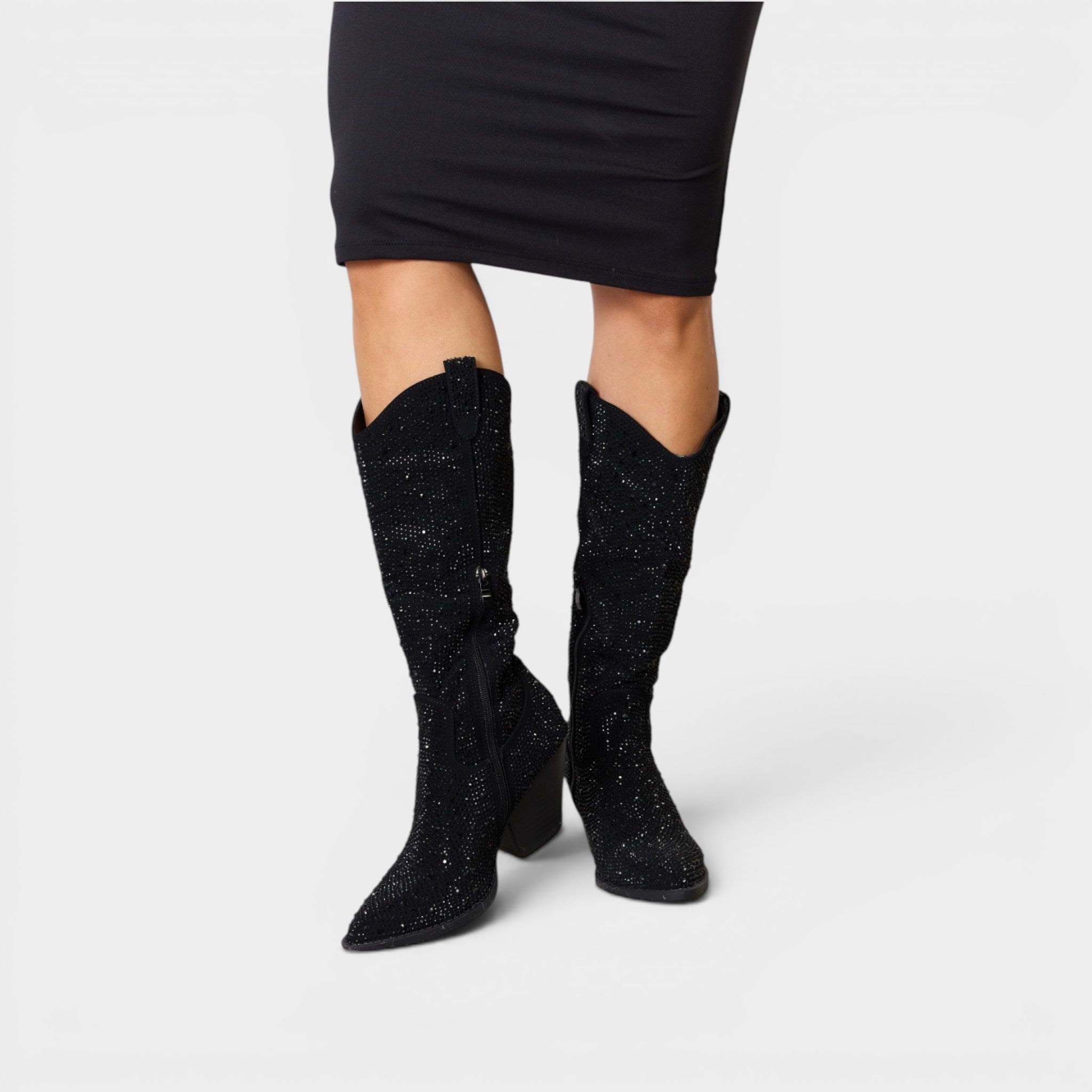 Black glittery knee-high boots worn with a black dress on a light gray background
