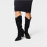 Black glittery knee-high boots worn with a black dress on a light gray background