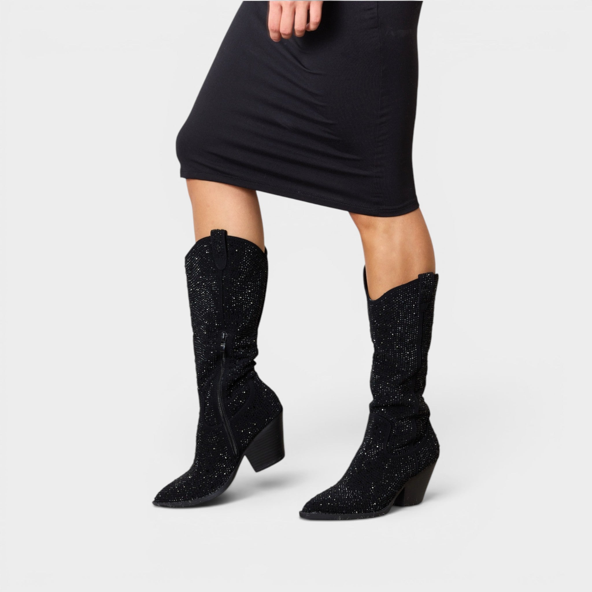 Black glittery knee-high boots worn with a black dress on a white background