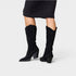 Black glittery knee-high boots worn with a black dress on a light gray background