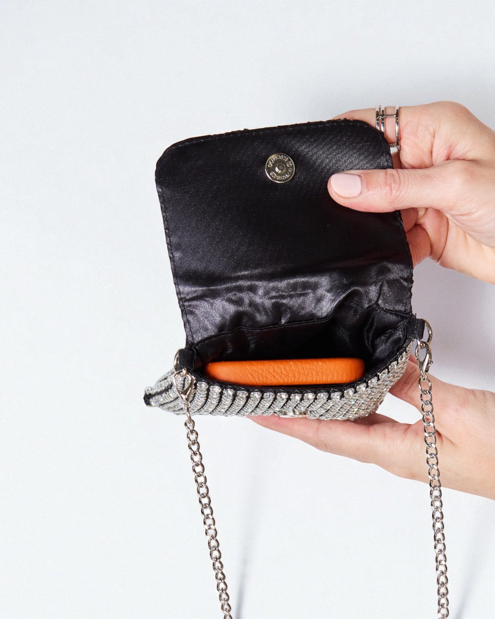 Black handbag with chain strap held by a hand on a white background