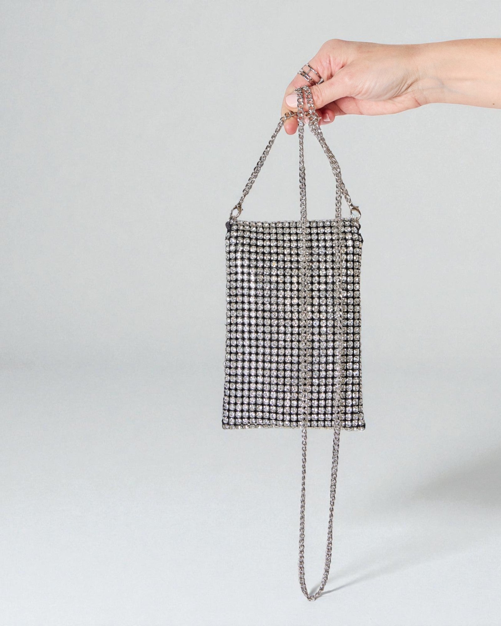Hand holding a small black and white checkered bag with a chain strap on a light gray background