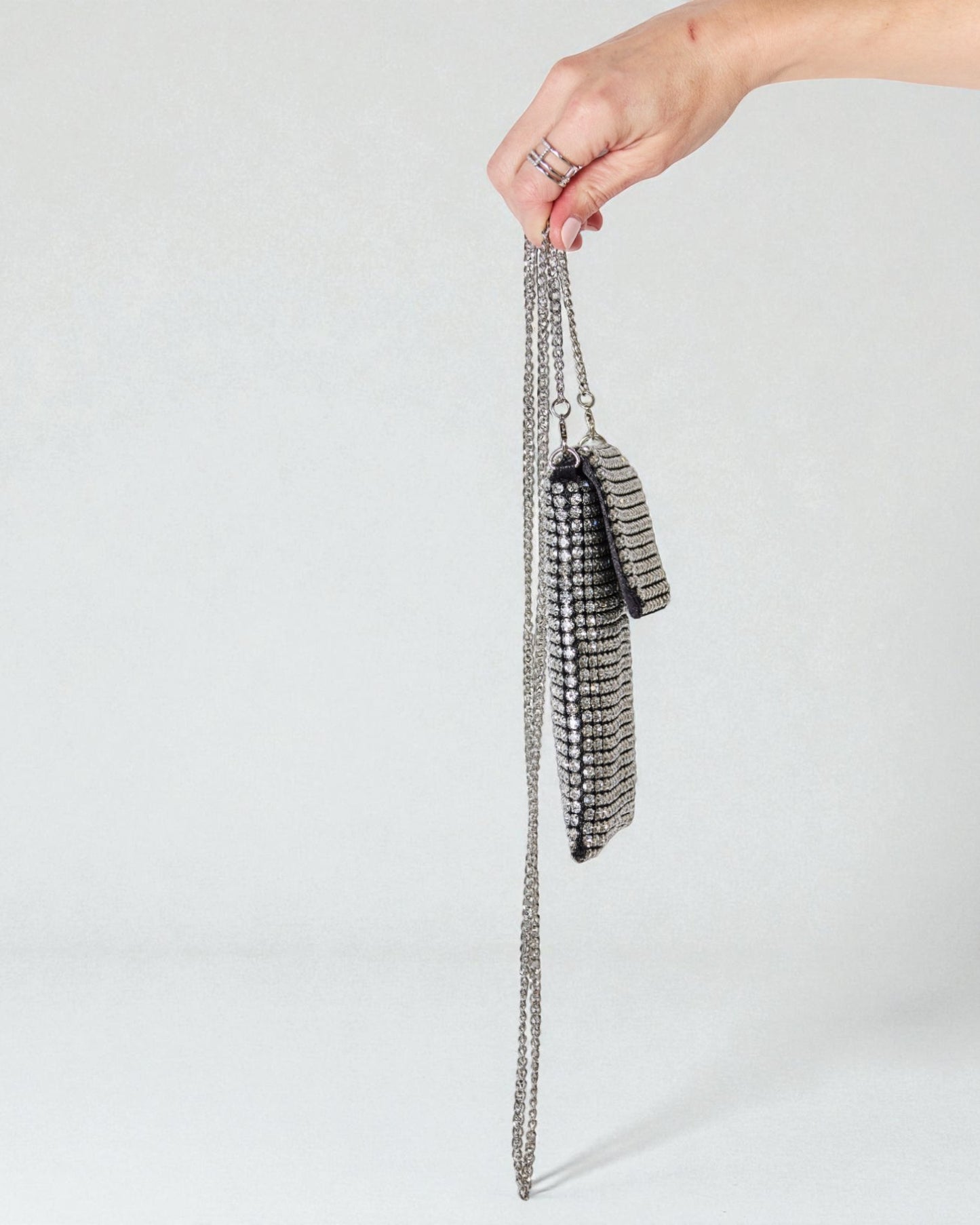 Hand holding a silver chain bag against a light gray background