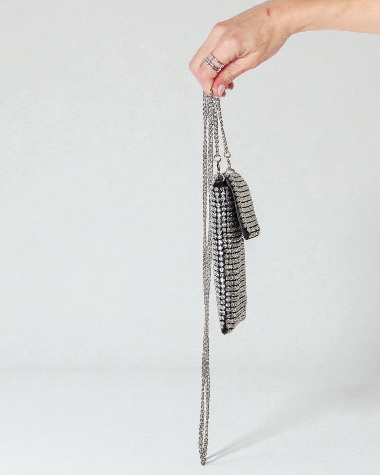 Hand holding a silver chain bag against a light gray background