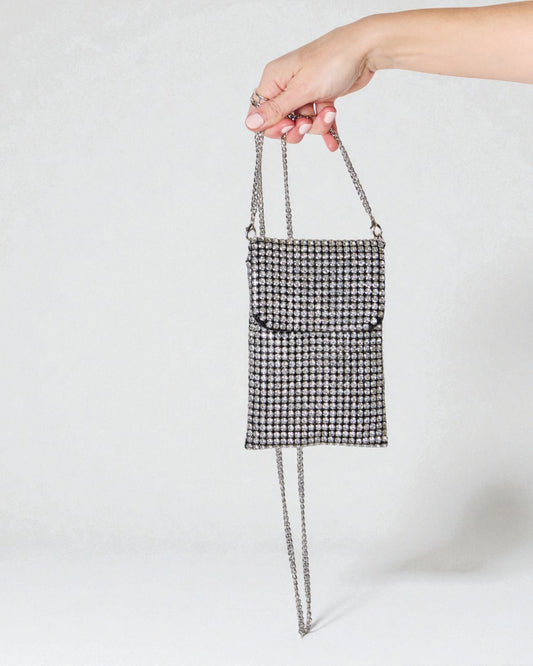 Hand holding a small black and white patterned handbag with a chain strap against a light gray background