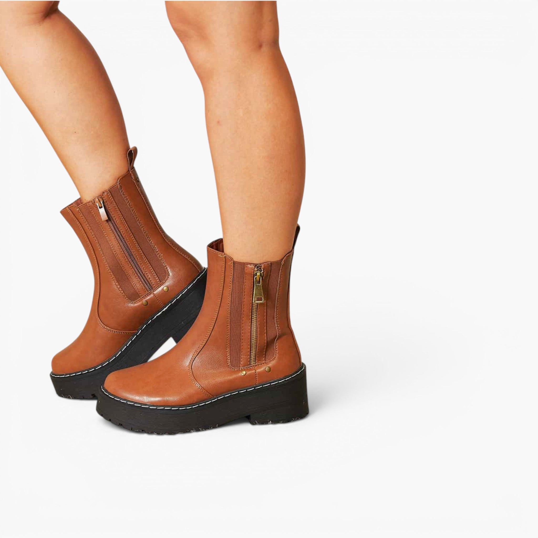 A pair of brown leather ankle boots with black platform soles and side zippers, shown on a model's feet against a plain white background.