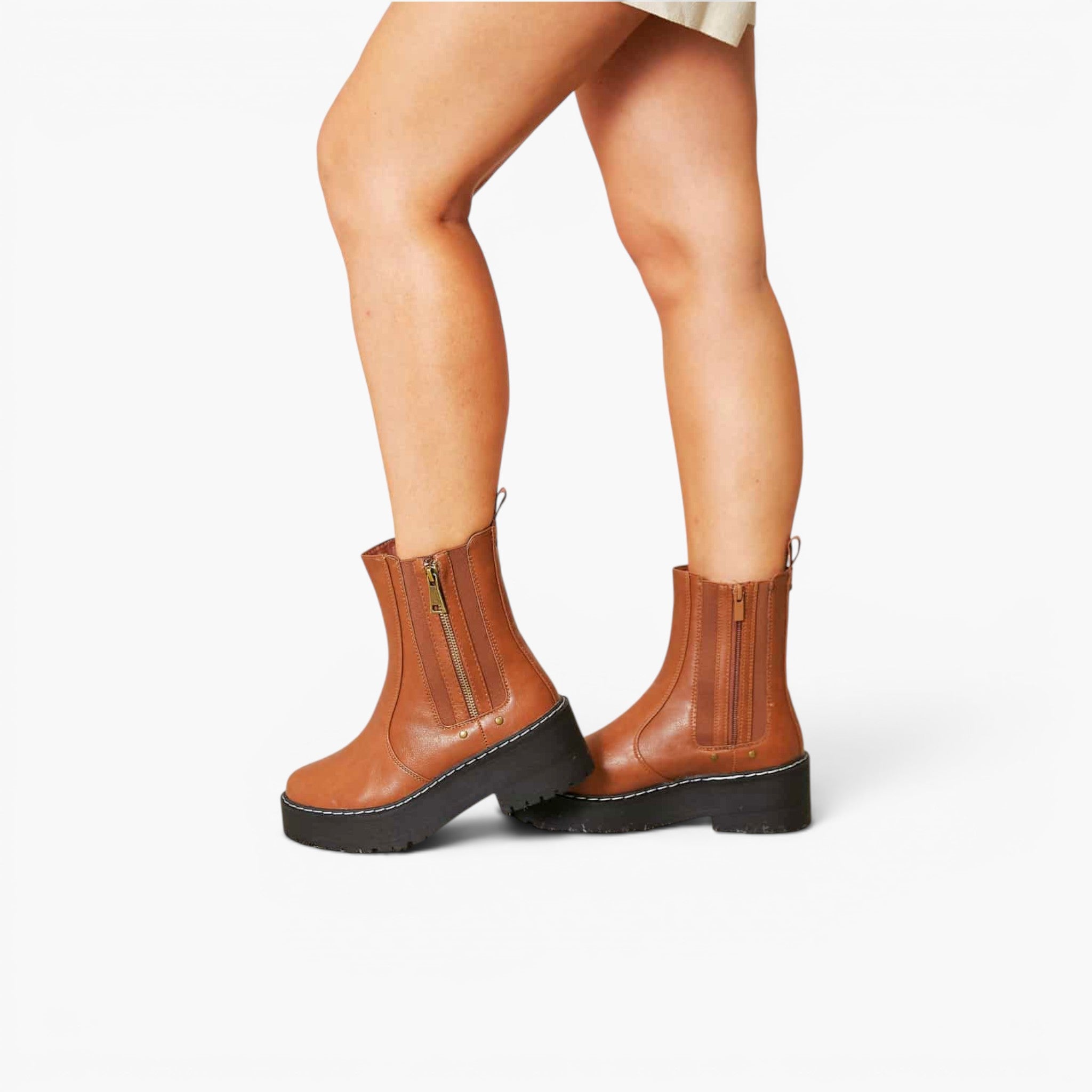 A pair of women's brown leather ankle boots with black platform soles and side zippers, shown on a model's feet against a light gray studio background.