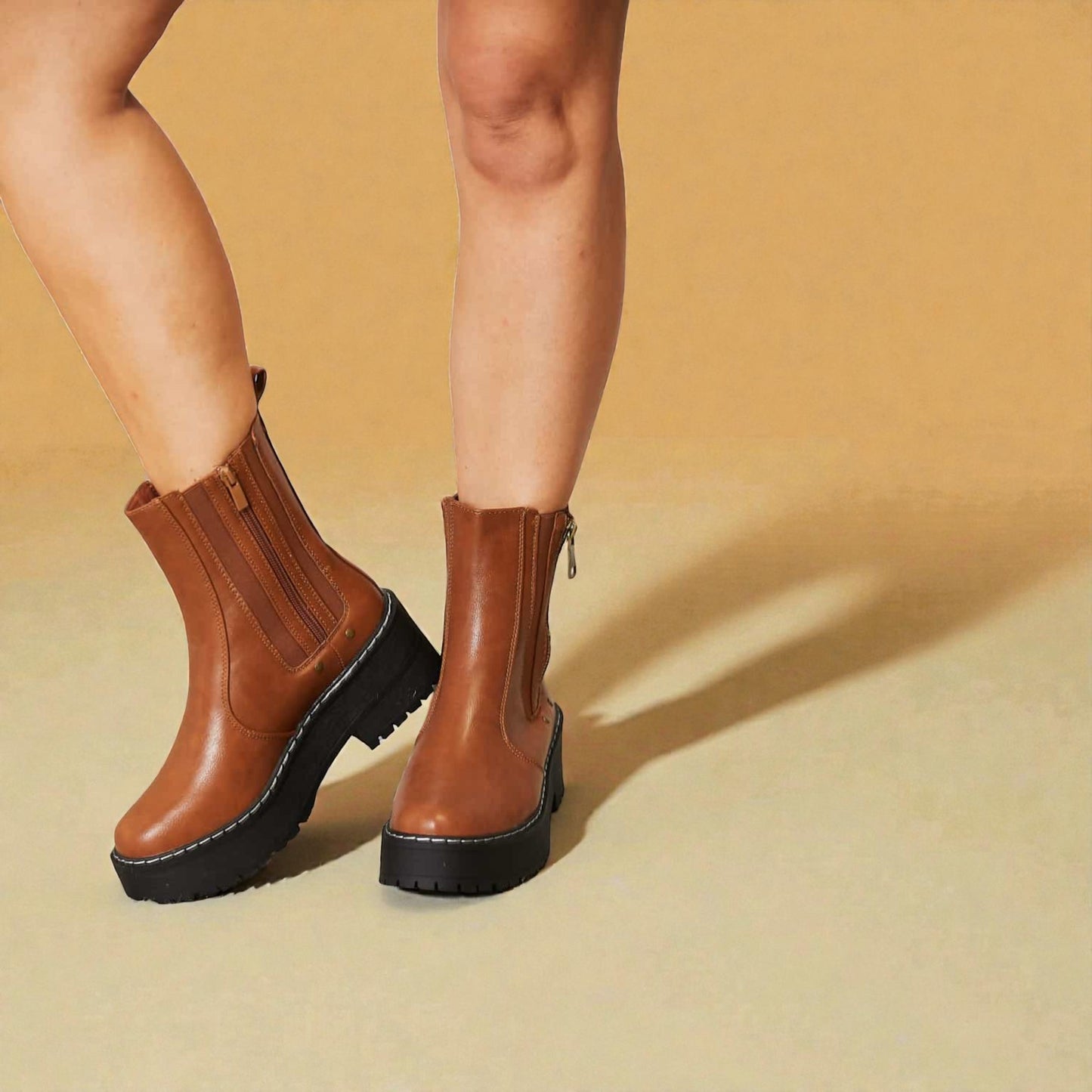 Brown ankle boots worn by a person on a beige background