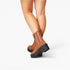 A pair of women's ankle boots in tan brown leather with black platform soles, shown on a model's feet against a light gray studio background.