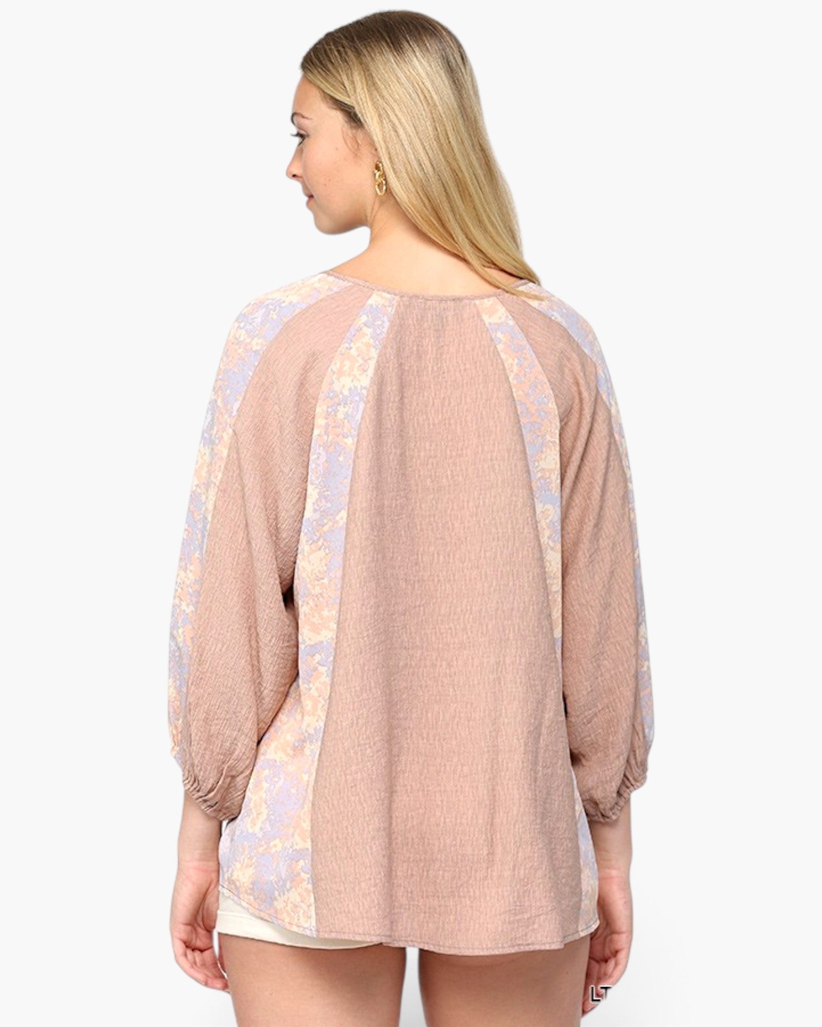 A woman shown from the back wearing a loose, long-sleeve top with a textured dusty pink body and light lavender floral patterned shoulder and side panels, set against a plain white background.