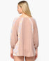 A woman shown from the back wearing a loose, long-sleeve top with a textured dusty pink body and light lavender floral patterned shoulder and side panels, set against a plain white background.