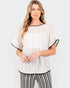 A woman modeling a loose, short-sleeve textured knit top in off-white with black trim, paired with black-and-white striped pants, against a light gray studio background.