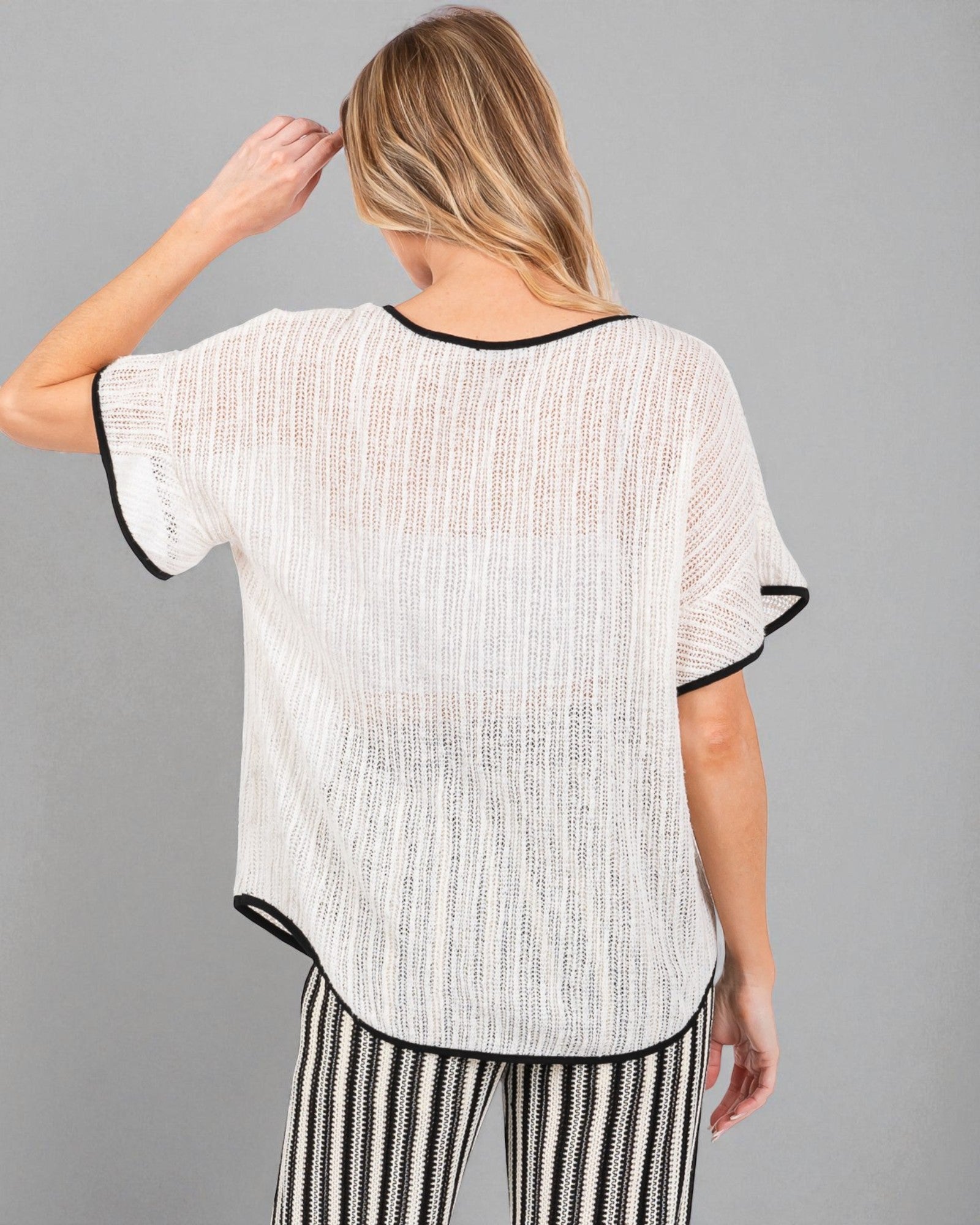 Woman wearing a white and black patterned top with black trim on a gray background