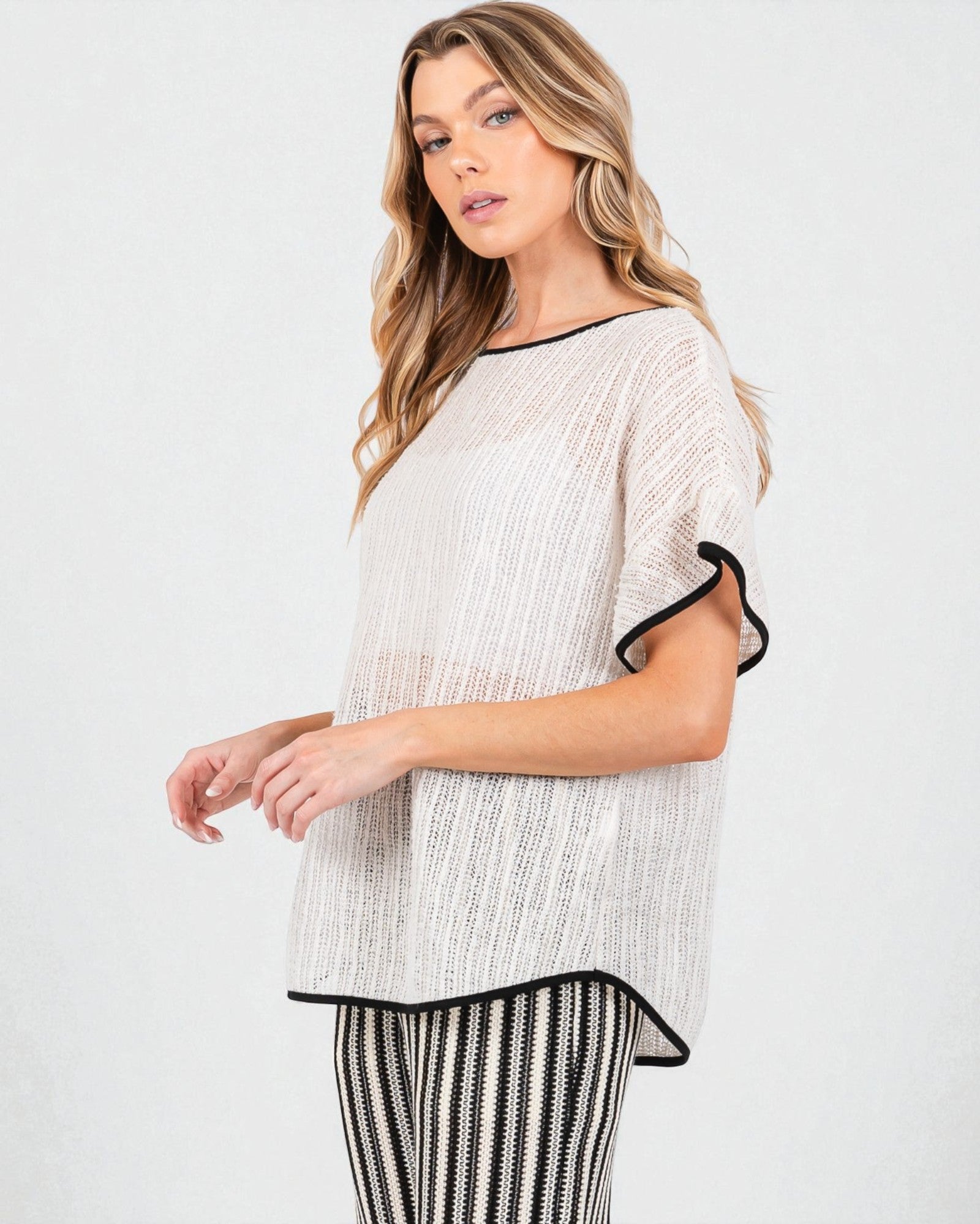 Woman wearing a beige knit top with black trim on a white background