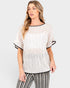 A woman wearing a white textured short-sleeve top with black trim and black-and-white striped pants, photographed against a light gray studio background.
