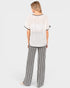 A woman shown from the back wearing a two-piece lounge set consisting of a white textured short-sleeve top with black trim and black-and-white vertically striped wide-leg pants, set against a solid light gray background.