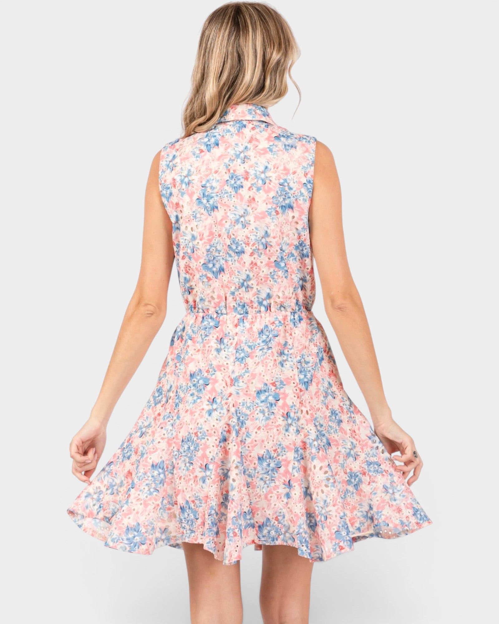 A woman shown from the back wearing a sleeveless collared fit-and-flare dress with a pink, blue, and white floral pattern, set against a solid light gray background.