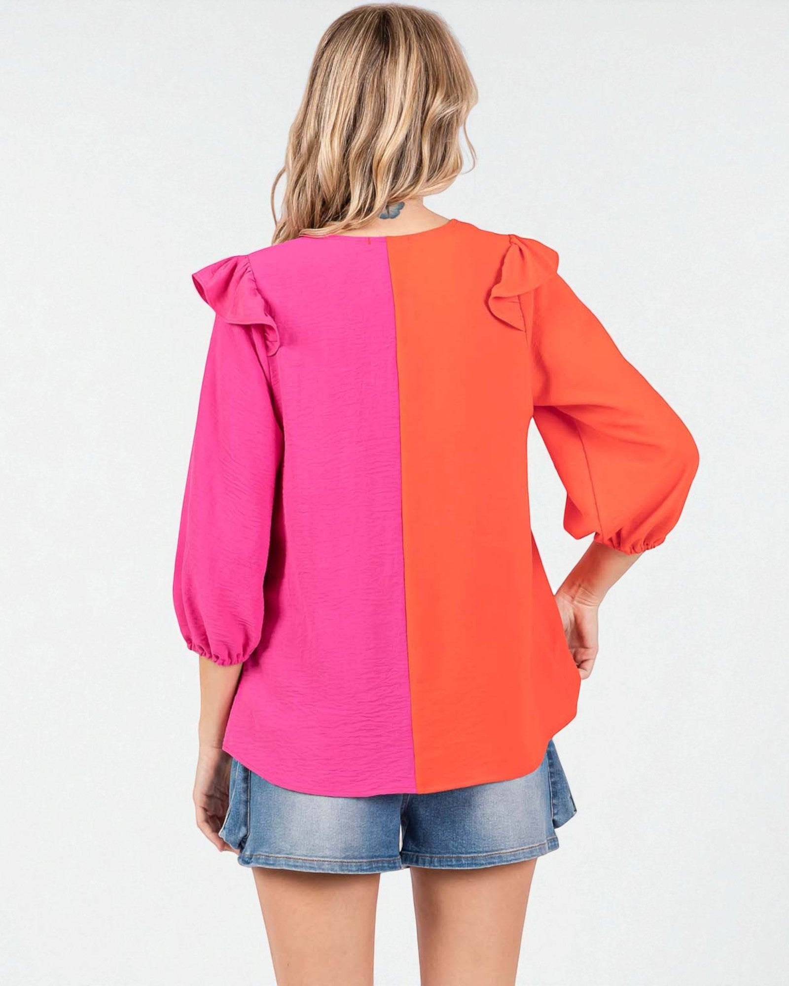 Woman wearing a pink and orange blouse with ruffled sleeves on a white background
