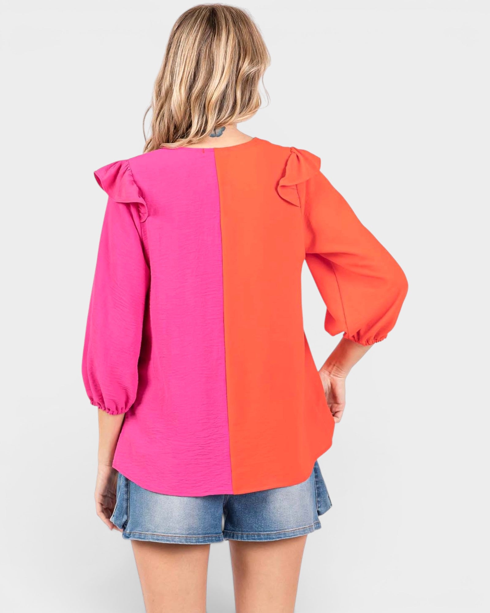 Woman wearing a pink and orange color-blocked blouse with denim shorts on a white background