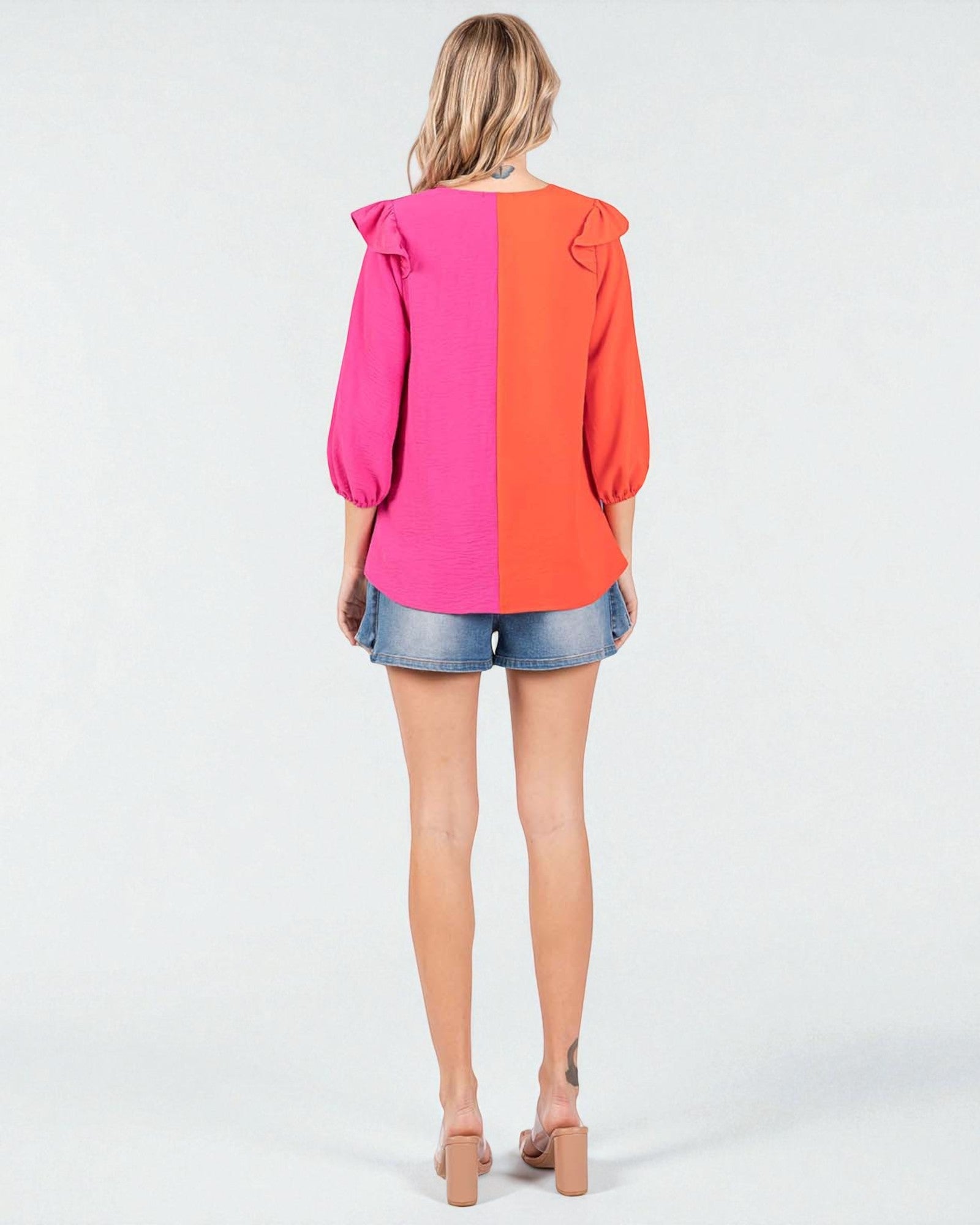 Woman wearing a two-tone pink and orange blouse with denim shorts on a white background