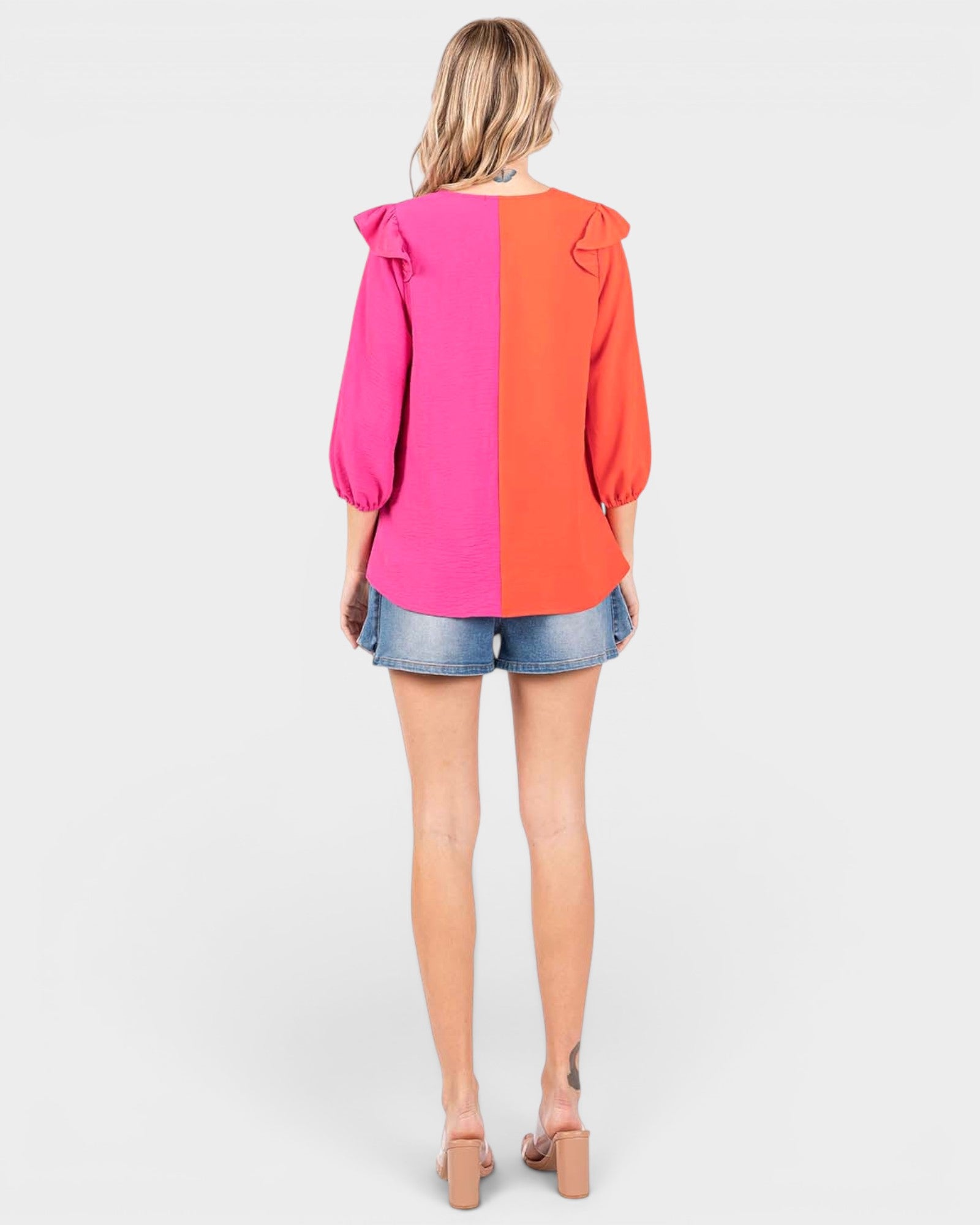 Woman wearing a two-tone pink and orange blouse with denim shorts on a white background