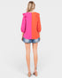 Woman wearing a two-tone pink and orange blouse with denim shorts on a white background