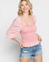 Woman wearing a pink blouse with puff sleeves and denim shorts on a light gray background