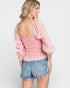 Woman wearing a pink blouse with ruffled sleeves and denim shorts on a white background