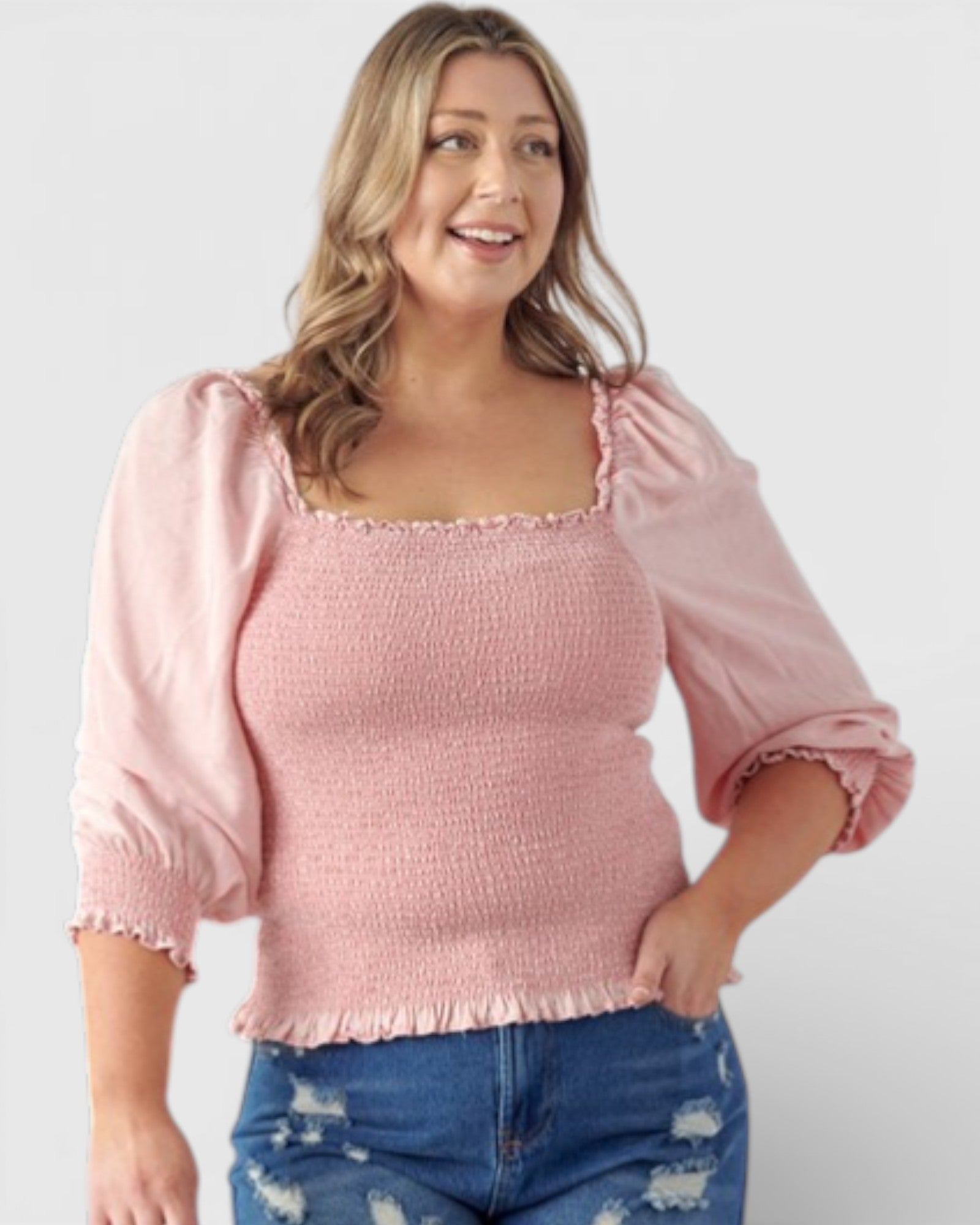 Woman wearing a pink top with ruffled sleeves and blue jeans on a plain background