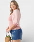 Woman wearing a pink blouse and denim shorts holding a basket with a white background