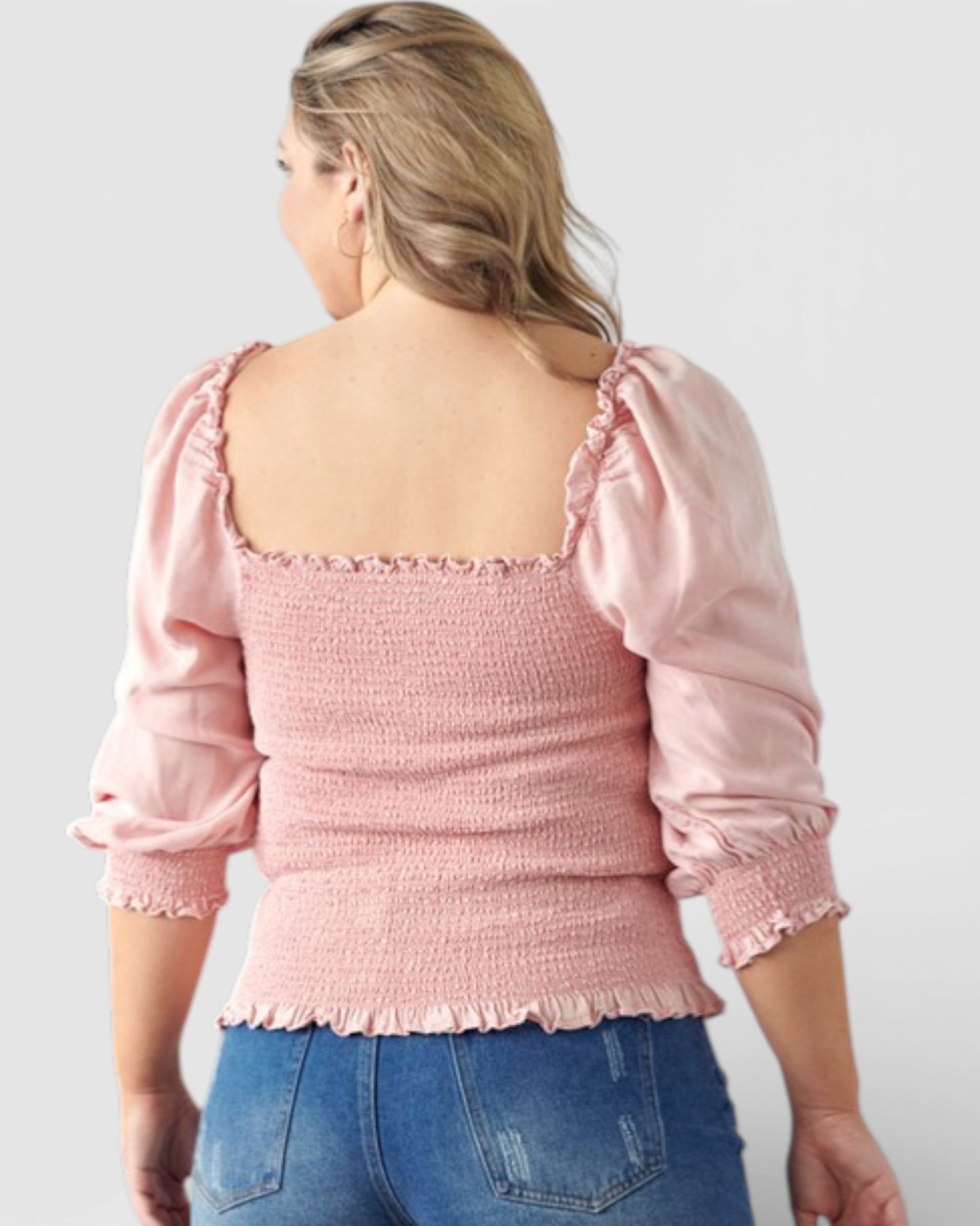 Person wearing a pink blouse with puffed sleeves and blue jeans on a plain background