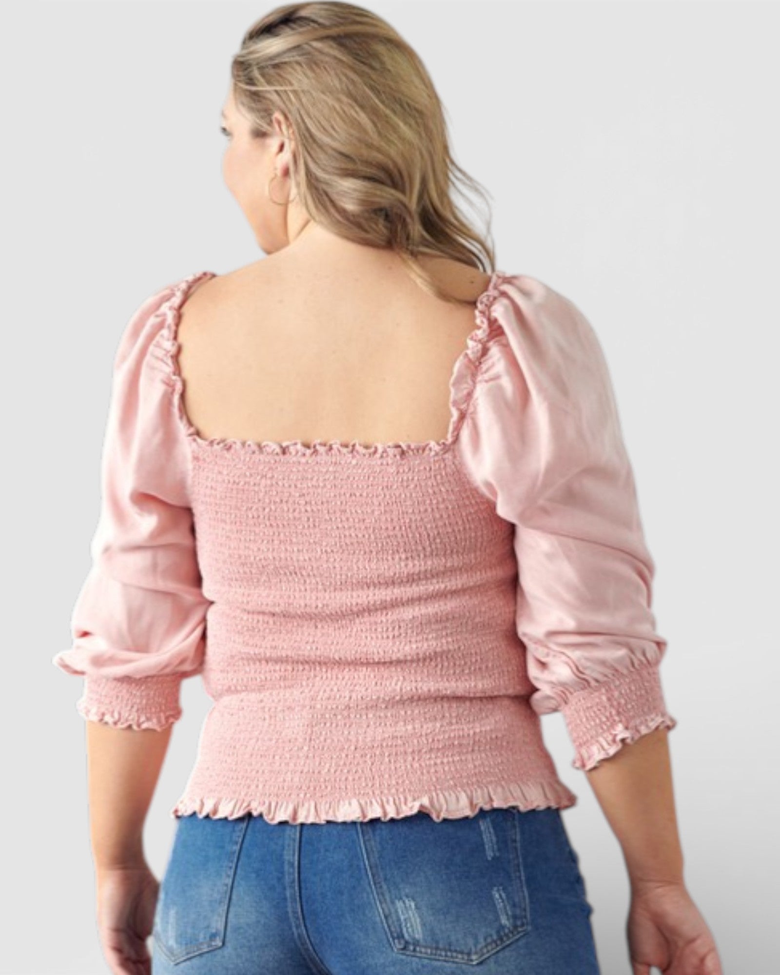 Person wearing a pink blouse with puffed sleeves and blue jeans on a plain background