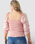 Person wearing a pink blouse with puffed sleeves and blue jeans on a plain background