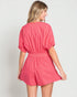 Woman wearing a pink romper against a plain background