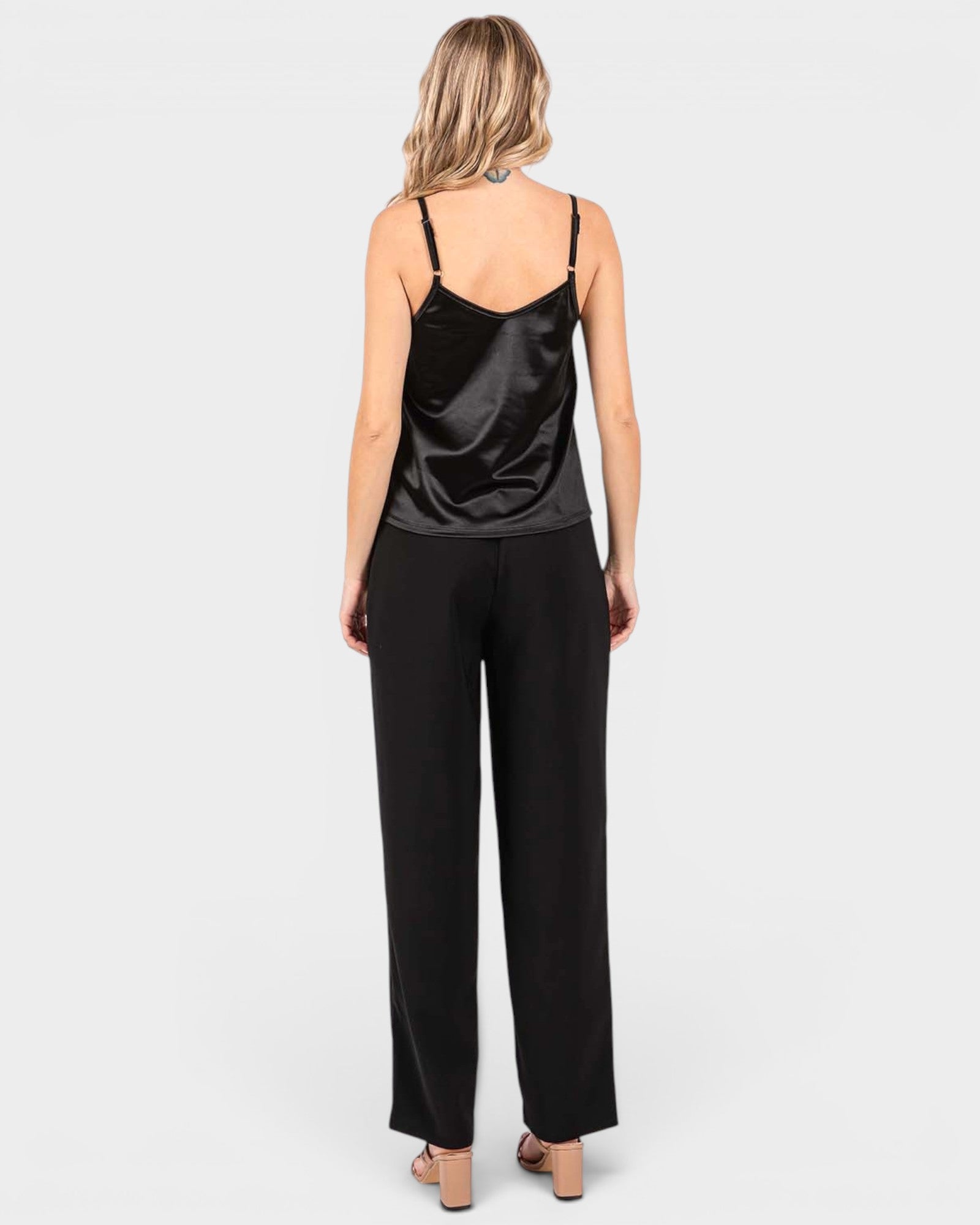 A woman shown from the back wearing a black satin camisole top and black wide-leg trousers against a light gray studio background.