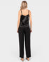 A woman shown from the back wearing a black satin camisole top and black wide-leg trousers against a light gray studio background.