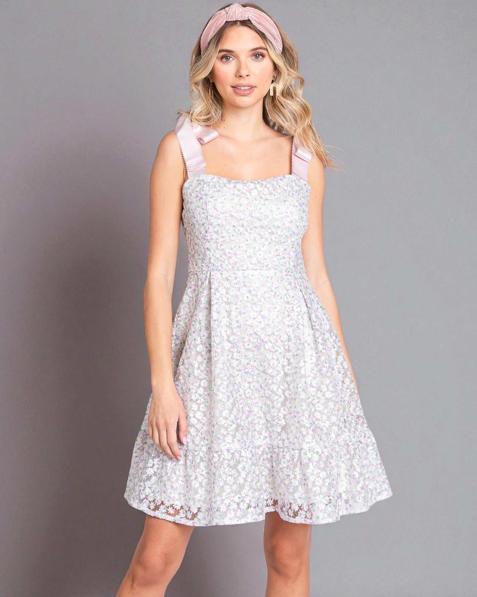 Woman wearing a white lace dress with pink straps against a gray background