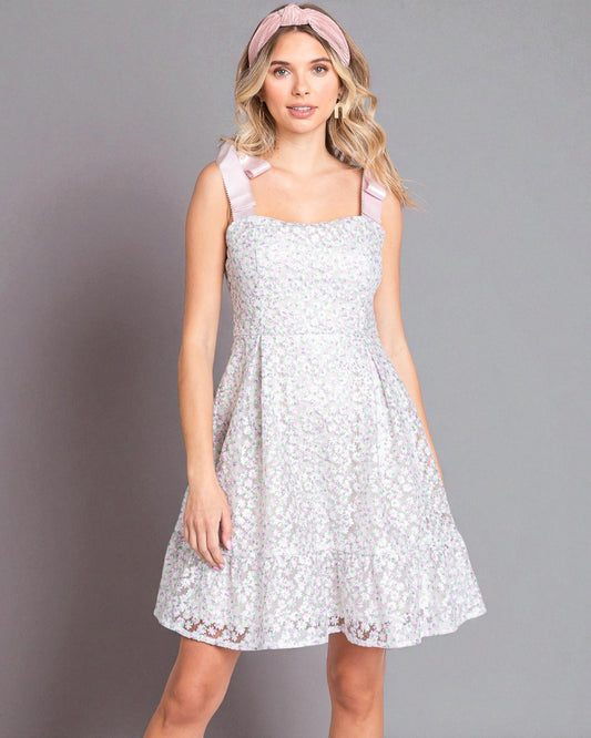 Woman wearing a white lace dress with pink straps against a gray background