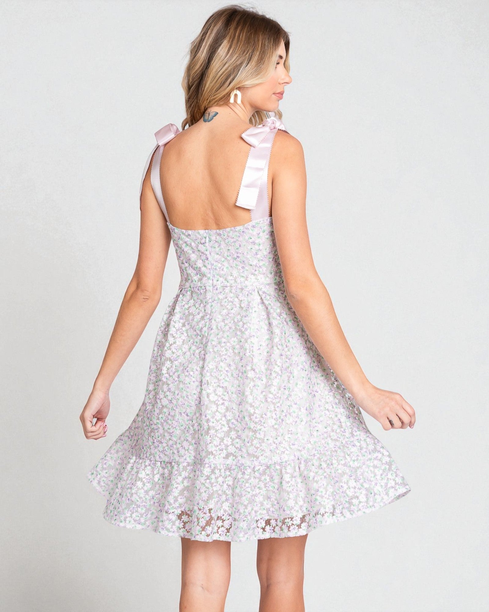 Woman wearing a white lace dress with bow straps on a plain background