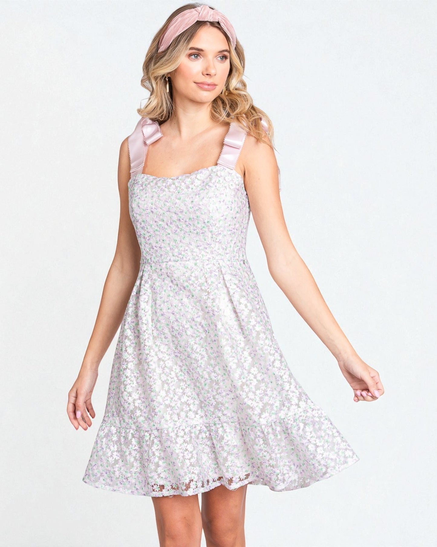 Woman wearing a white floral dress with pink straps on a light gray background