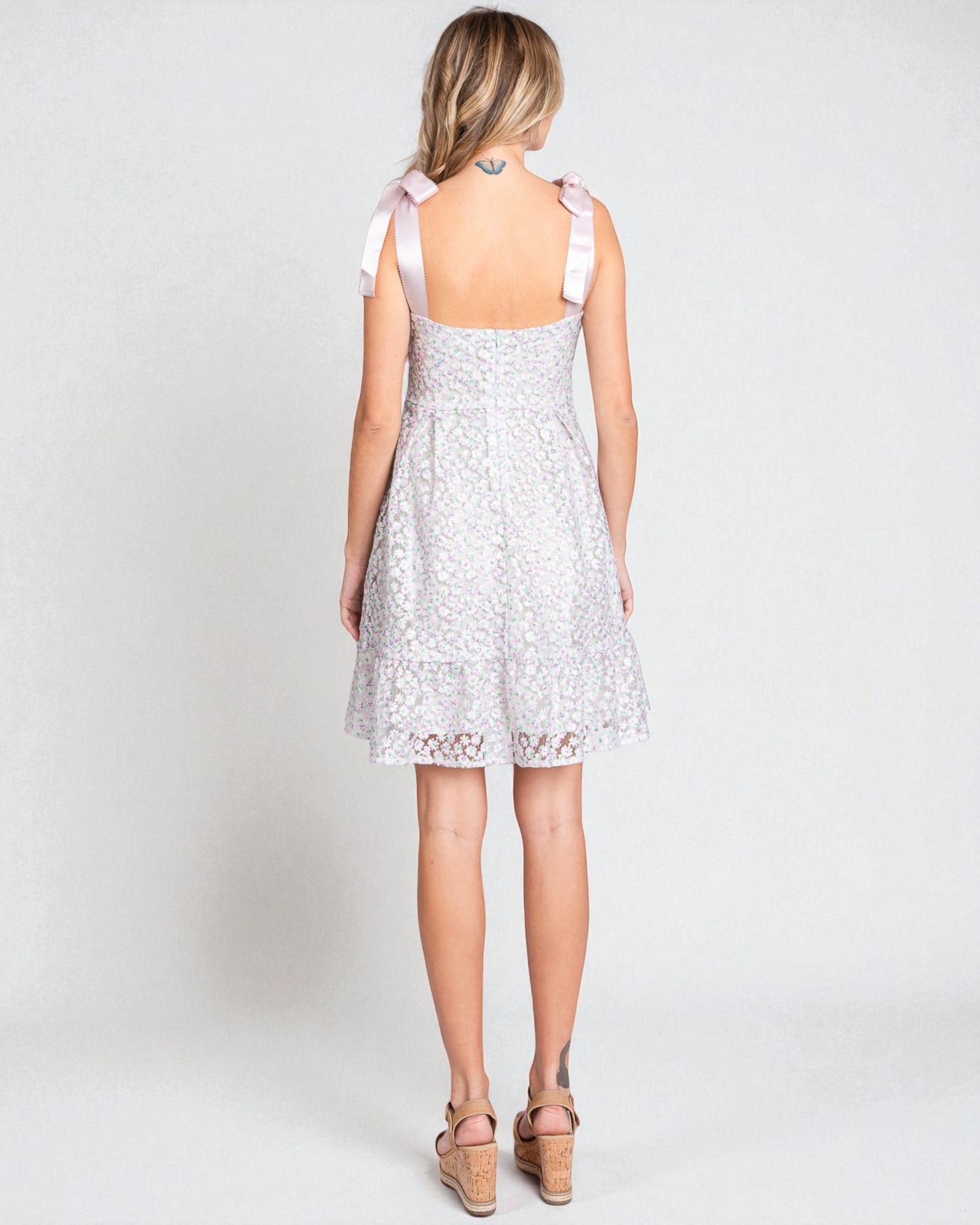 Woman wearing a white lace dress with pink straps on a plain background