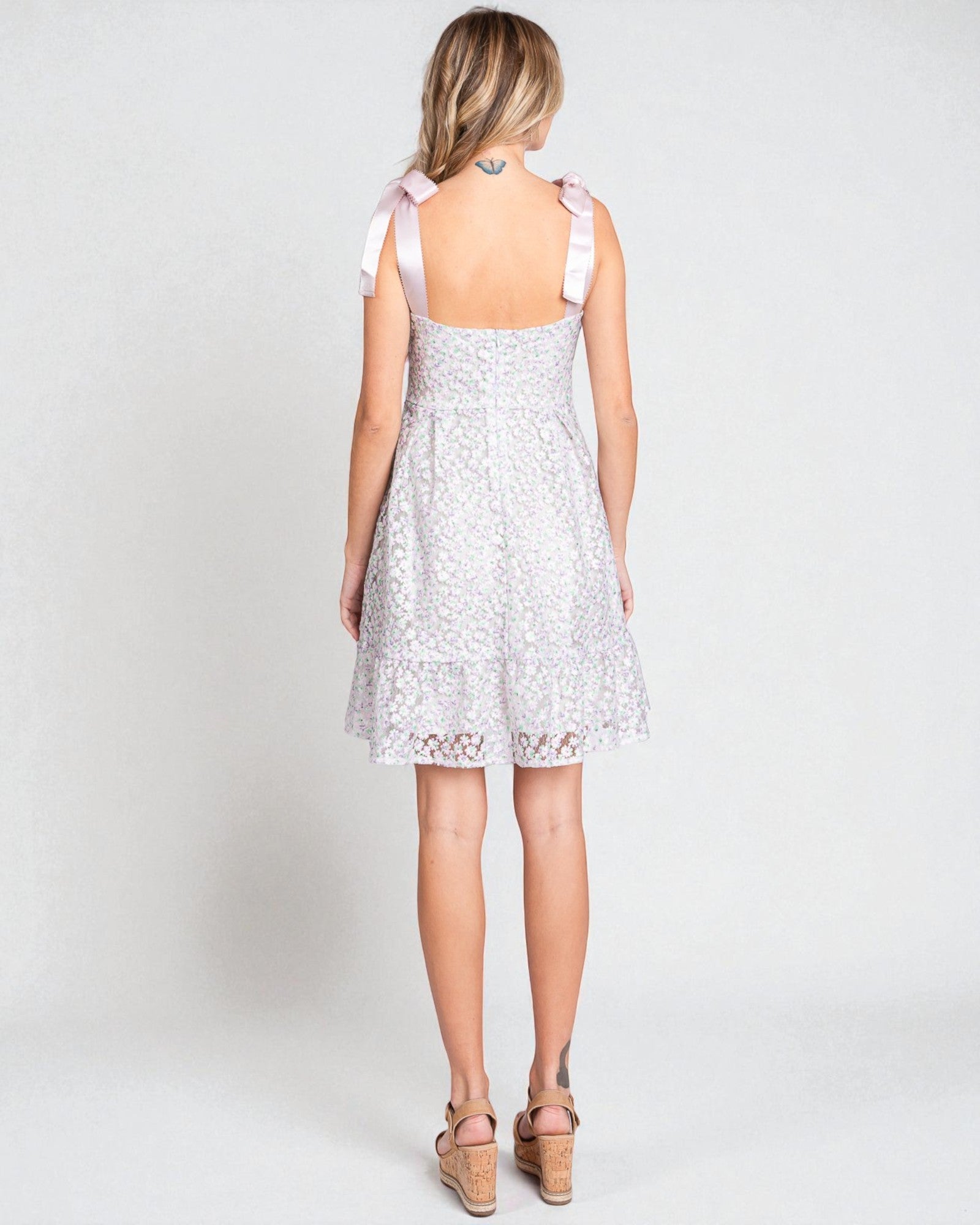 Woman wearing a white lace dress with pink straps on a plain background