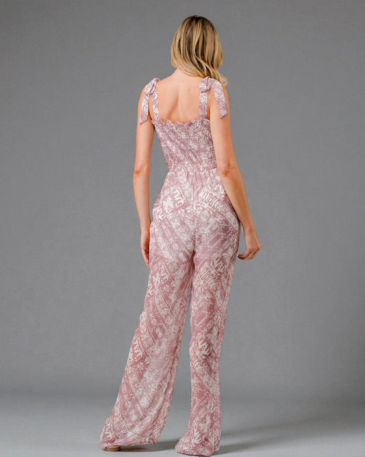 Woman wearing a pink lace jumpsuit against a gray background