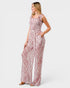 A woman modeling a sleeveless jumpsuit with a pink and white abstract pattern, photographed against a light gray studio background.